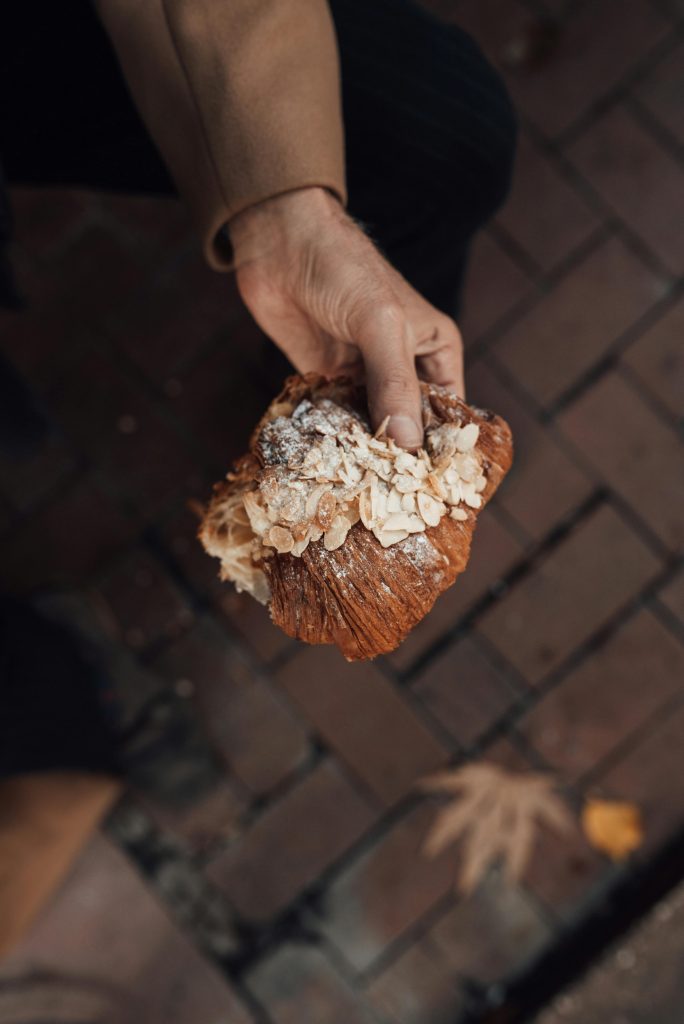 Close-up of a hand holding an almond croissant on a brick path, perfect for food and lifestyle themes.