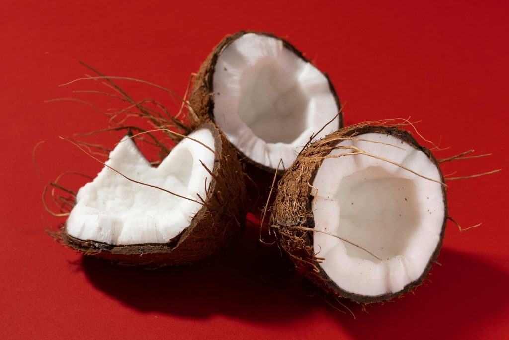 Three fresh coconut halves on a vibrant red background, showcasing their texture and natural detail.